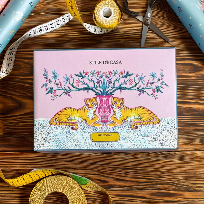 May include: A pink gift box with a blue border features a floral design with two tigers flanking a vase. The text "STILE D'CASA" and "GE LIVING" are printed on the box.
