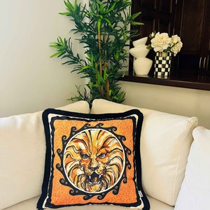May include: A decorative throw pillow with a black trim features a lion's face in a circular frame with a black and orange background.