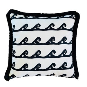 May include: A white pillow with a black wave pattern and black fringe trim. The waves are stylized and have small circles inside them.