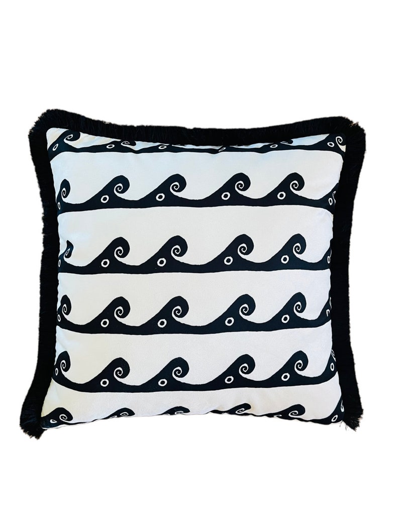 May include: A white pillow with a black wave pattern and black fringe trim. The waves are stylized and have small circles inside them.