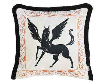 May include: A white pillow with a black winged horse design inside an orange and white frame. The pillow has a black fringe border.