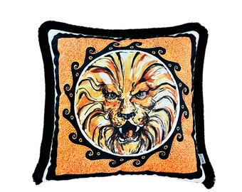 May include: Orange and black throw pillow with a lion face illustration in a circular frame. The lion has a fierce expression with a wide open mouth and sharp teeth.