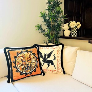 May include: Two decorative throw pillows with black trim. One pillow features a black and white illustration of a winged horse. The other pillow features a black and orange illustration of a lion's head.