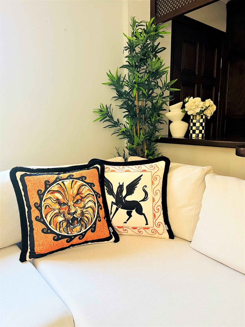 May include: Two decorative throw pillows with black trim. One pillow features a black and white illustration of a winged horse. The other pillow features a black and orange illustration of a lion's head.