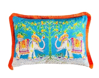 Peut inclure: Coussin rectangulaire décoratif avec un fond turquoise vif. Le coussin présente un motif symétrique d'éléphants blancs avec des couvertures colorées à motifs, un arbre central avec des fruits et une bordure à franges orange.