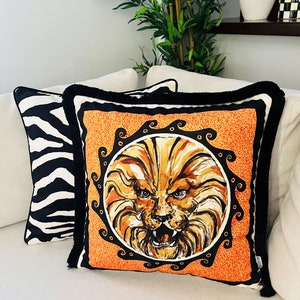 May include: Two decorative throw pillows, one with a black and white zebra print and the other with a bright orange background and a black and gold lion face illustration.