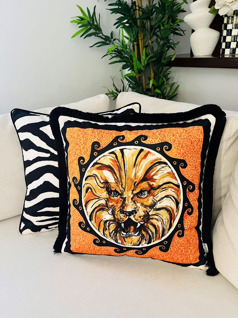 May include: Two decorative throw pillows, one with a black and white zebra print and the other with a bright orange background and a black and gold lion face illustration.