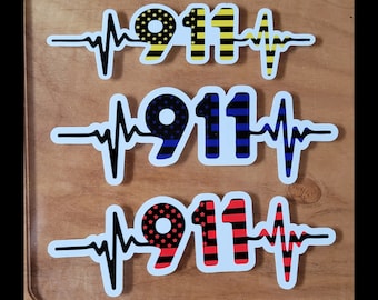 Pode incluir: Três adesivos com o número "911" em várias cores e padrões, cada um sobreposto com uma linha de batimento cardíaco preta. O adesivo superior tem listras amarelas e pretas, o do meio tem listras azuis e o inferior tem listras vermelhas.