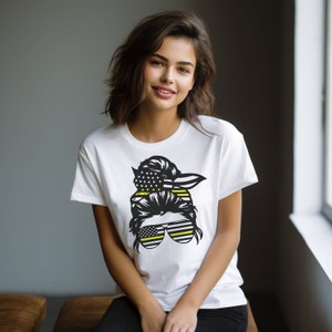 May include: White t-shirt with a black and yellow graphic of a woman's hair in a bun with an American flag and a thin yellow line flag bandana. The graphic also includes sunglasses with a thin yellow line flag design.