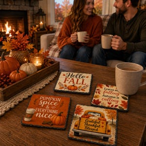 May include: Four square stone coasters featuring autumn-themed designs. One reads Hello Fall with a pumpkin, another says Pumpkin spice & everything nice, one says Leaves are falling Autumn is calling, and the last shows a truck with Grateful Thankful Blessed.