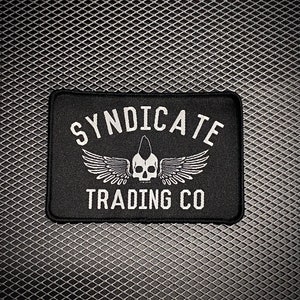 May include: Black and white embroidered patch with the text "Syndicate Trading Co." and a skull with wings.