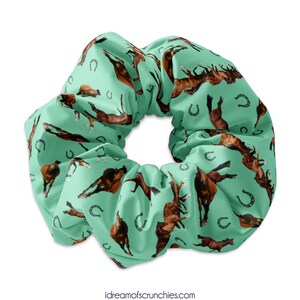 May include: A green scrunchie with a repeating pattern of brown horses and horseshoes.
