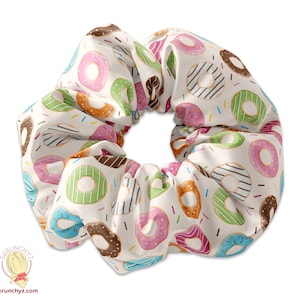 May include: A white scrunchie with a donut pattern. The donuts are in various colors, including pink, green, blue, and brown. The donuts have sprinkles and chocolate frosting.