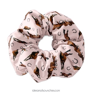 May include: A pink scrunchie with a repeating pattern of brown horses and silver horseshoes.