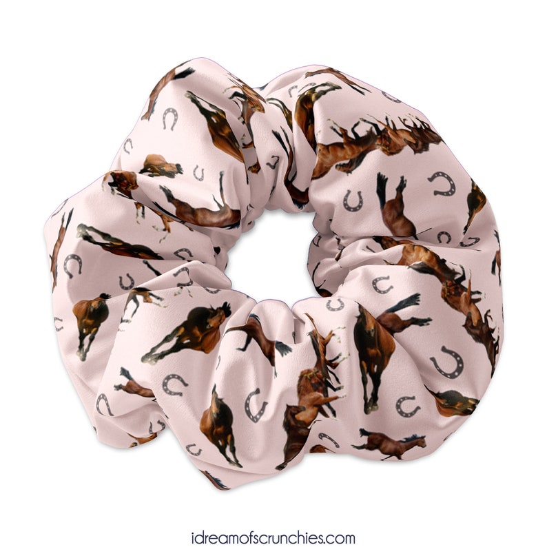 May include: A pink scrunchie with a repeating pattern of brown horses and silver horseshoes.