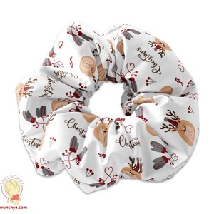 Könnte beinhalten: Ein weißer Scrunchie mit einem sich wiederholenden Muster aus roten und braunen Rentieren, Stechpalmen und dem Wort "Weihnachten".