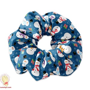 Könnte beinhalten: Blauer Scrunchie mit einem sich wiederholenden Muster aus Schneemännern, die Hüte und Schals tragen, Geschenke halten und von Schneeflocken umgeben sind.