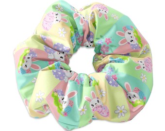 May include: A pastel green, pink and yellow scrunchie with a repeating pattern of white bunnies holding Easter eggs. The bunnies are surrounded by flowers and green leaves.