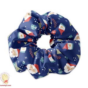 Könnte beinhalten: Ein marineblaues Haargummi mit einem sich wiederholenden Weihnachtsmuster. Das Design umfasst Weihnachtsmann-Gesichter, verpackte Geschenke, Weihnachtsbäume, Schneeflocken und Zweige. Das Haargummi ist aus einem weichen, seidigen Material gefertigt.