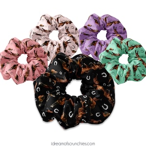 Puede incluir: Cinco scrunchies coloridos con un patrón de caballo y herradura. Los scrunchies son de color rosa, morado, verde, negro y marrón.
