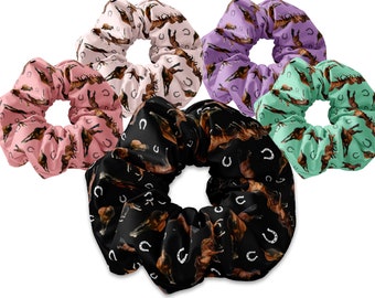 May include: Five colorful scrunchies with a horse and horseshoe pattern. The scrunchies are in pink, purple, green, black, and brown.