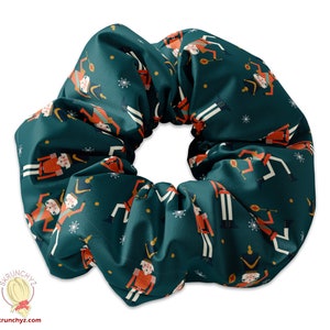 Könnte beinhalten: Ein türkisfarbener Scrunchie mit einem sich wiederholenden Muster aus illustrierten Nussknackerfiguren in Rot, Weiß und Braun. Die Nussknacker halten eine Trommel und einen Zuckerstock.