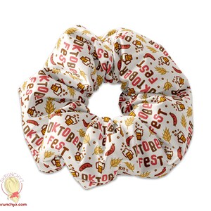 Könnte beinhalten: Ein weißer Scrunchie mit einem sich wiederholenden Muster aus Bierkrügen, Brezeln und dem Text "Oktoberfest".