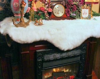 Könnte beinhalten: Ein weißer Kunstfellüberwurf, der über einem Kaminsims mit einem schwarzen und goldenen Kamineinsatz drapiert ist. Der Kamin ist angezündet und die Flammen sind sichtbar. Der Text "All I Want For Christmas" ist in Weiß auf schwarzem Hintergrund unterhalb des Kamins geschrieben. Der Text "FUR ACCENTS" ist in Türkis auf schwarzem Hintergrund unterhalb des Textes "All I Want For Christmas" geschrieben.