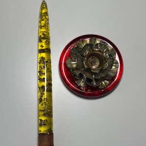May include: A yellow candle with gold flecks in a red and gold metal candle holder shaped like a flower.