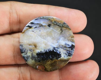 May include: A circular polished gemstone cabochon featuring a translucent white and cream base with intricate black dendritic fern-like inclusions and earthy brown patches throughout the stone surface, displaying a smooth and glossy finish.