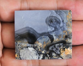 Puede incluir: Una losa pulida de ágata gris, negra y dorada con patrones de remolino. La ágata tiene una superficie lisa y pulida y es una piedra natural.