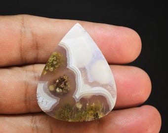 May include: A teardrop-shaped polished gemstone featuring a translucent white and pale lavender base with intricate, swirling white banding and embedded mossy green and brown mineral inclusions throughout the surface of the stone.