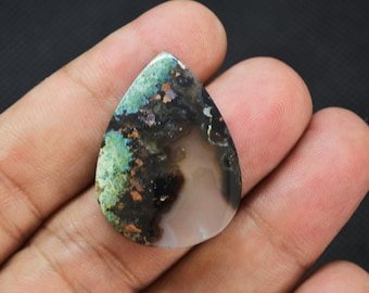 May include: A teardrop-shaped cabochon gemstone featuring a mix of translucent light brown, opaque black, and vibrant green mineral inclusions. The polished surface displays a smooth, rounded top with a distinct color gradient.