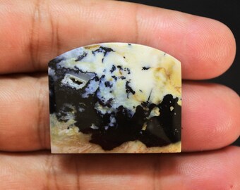 May include: A polished, flat, semi-circular gemstone cabochon featuring a marbled pattern of creamy white, tan, and deep black colors. The stone displays intricate dendritic inclusions and a small, textured crystalline cavity on the left side.
