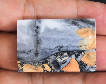 Puede incluir: Una losa rectangular de piedra pulida con un patrón único de blanco, gris, negro y naranja. La piedra tiene un aspecto en capas, marmoleado con una textura rugosa.