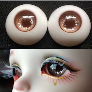 May include: Two brown and white doll eyes with glitter accents. The eyes are closed and have a light brown iris with a dark brown pupil.