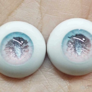 May include: Two white doll eyes with a blue, pink and silver glitter iris. The eyes are round and have a realistic appearance.