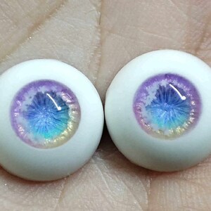 May include: Two white doll eyes with a purple, blue and iridescent glitter design.