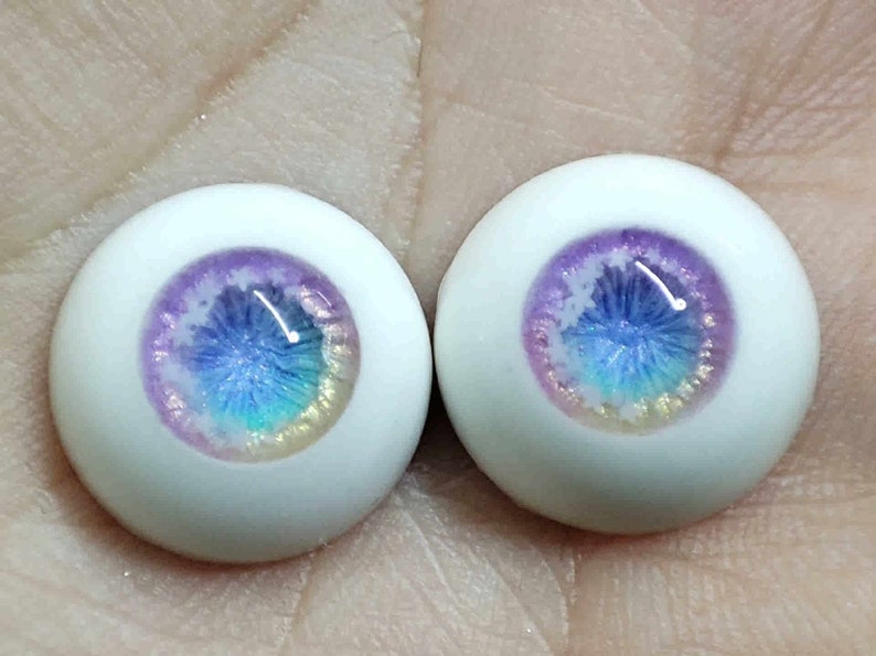 May include: Two white doll eyes with a purple, blue and iridescent glitter design.