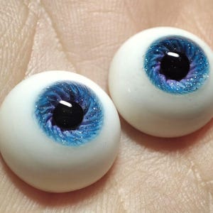 Puede incluir: Dos ojos de vidrio azul y morado realistas con purpurina. Los ojos son blancos por fuera y tienen una pupila negra.