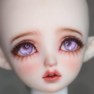 May include: A close-up of a doll's face with detailed features. The doll has light skin, delicate eyebrows, and long, dark eyelashes. The eyes are a striking purple with a reflective quality, and the lips are a soft, natural pink. The cheeks are blushed.