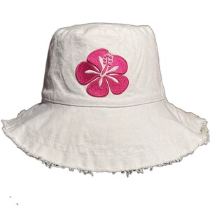 May include: White bucket hat with a pink hibiscus flower embroidered on the front. The hat has a frayed edge.