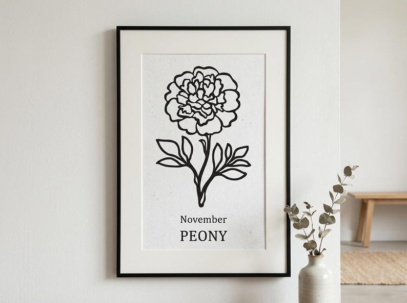 May include: Black framed art print featuring a black and white line drawing of a peony flower. The text "November PEONY" is printed below the flower. The artwork is displayed on a white wall.