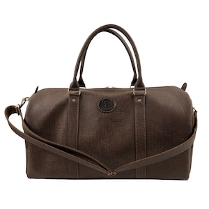 May include: A brown leather duffel bag with a shoulder strap and top handles. The bag has a textured surface and a brass zipper.