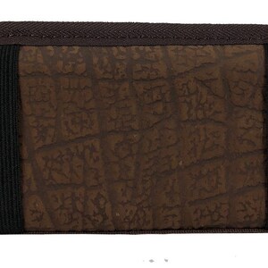 May include: A brown, semi-circular case with a textured surface and a dark brown border. Two black elastic straps are visible across the front. A black zipper is on the left side. The case appears to be made of durable material.
