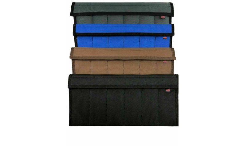 May include: A stack of rectangular, fabric pouches in various colors: dark green, blue, tan, and black. Each pouch has a flap closure and a small red and white tag. The pouches are designed with vertical stitching.