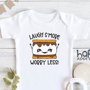 Pu&ograve; includere: Body bianco per neonato con un grafico di marshmallow arrostito e il testo "Laugh S'more Worry Less!"