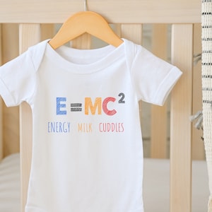 May include: White baby onesie with the text "E=MC2" in colorful letters. The text below reads "ENERGY MILK CUDDLES".