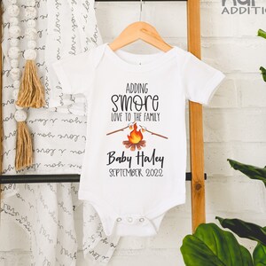 May include: White onesie with a campfire graphic and the text "Adding S'more Love to the Family" and "Baby Haley September 2022".