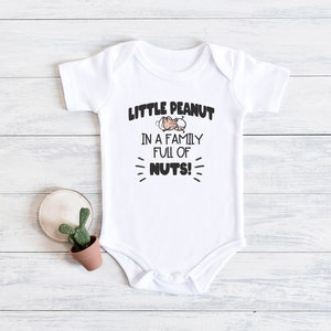 May include: White baby onesie with a cartoon peanut and the text "Little Peanut in a family full of nuts!"